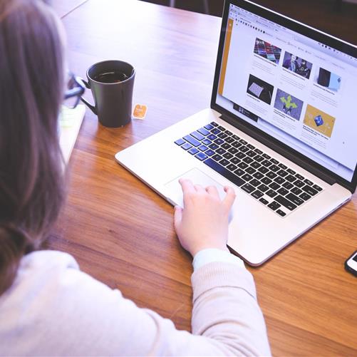 An employee using a laptop with online training thumbnails visible, sitting at a wooden desk with a cup of coffee nearby.