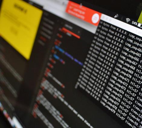 A computer screen displaying multiple panes of coding, scripts, and system information in a dimly lit room.