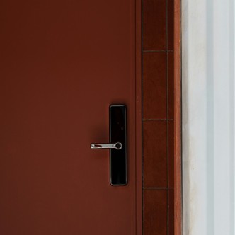 A closed dark red door with a sleek black handle and a small rectangular panel beside a tiled wall